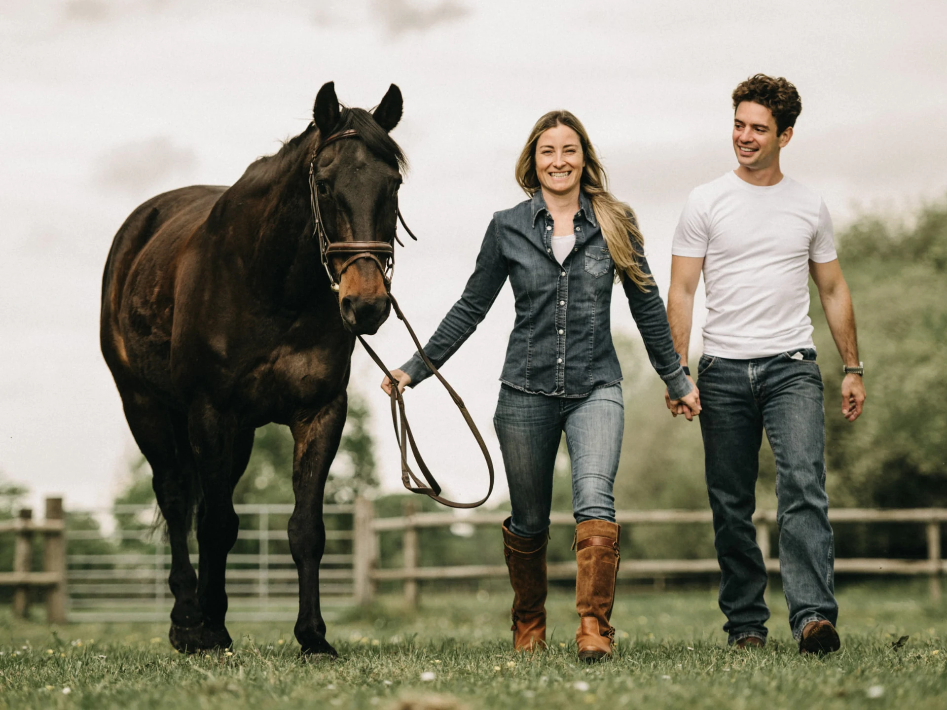 Audrey Kohli and Robin Cassidy walking hand in hand across a paddock, leading a dark bay horse